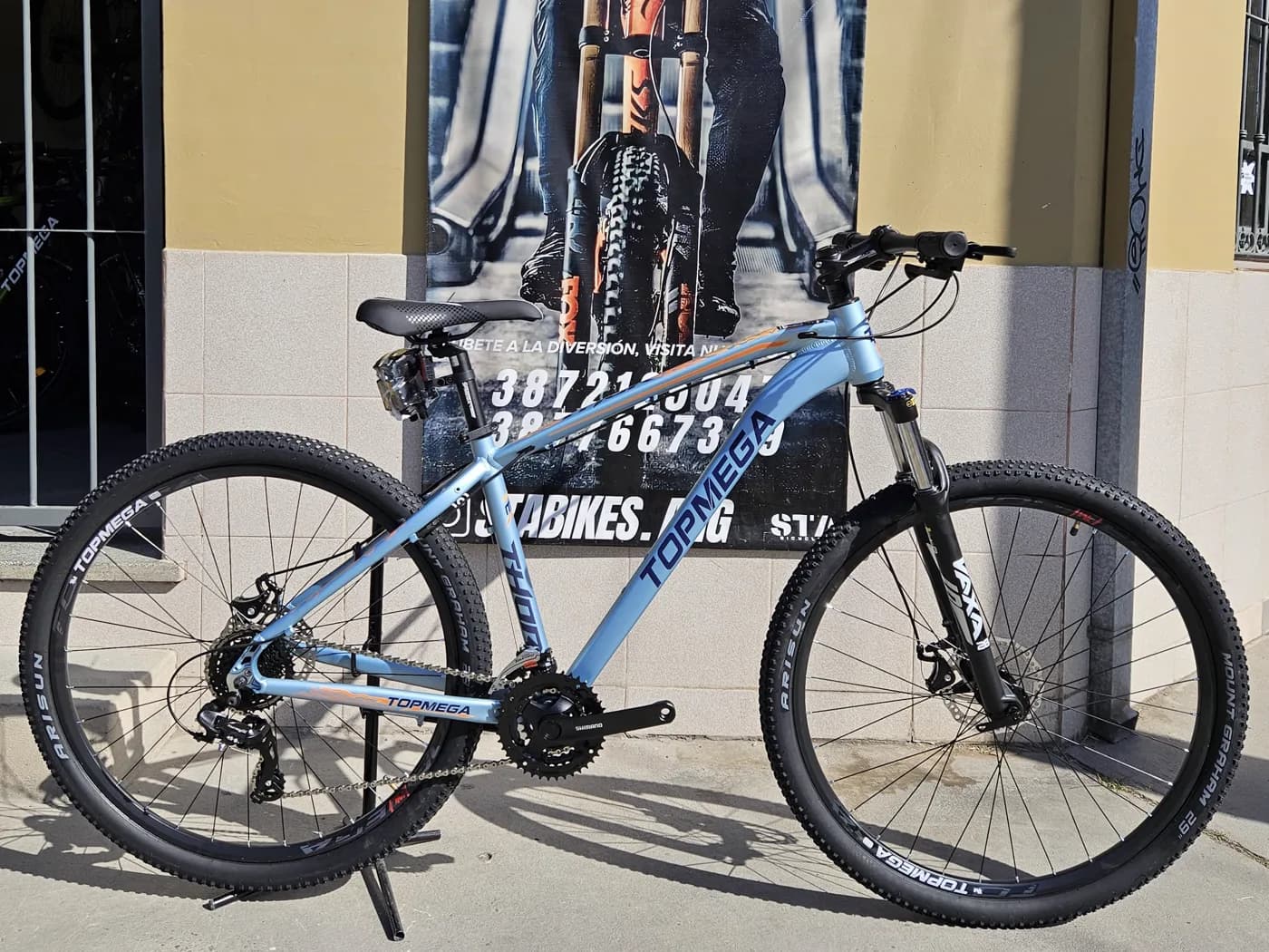 Bicicleta Topmega Thor celeste apoyada frente al local de STA BIKES